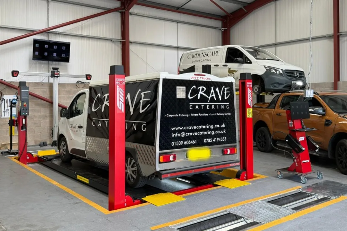 A commercial van on the four-post ramp beside the wheel alignment equipment